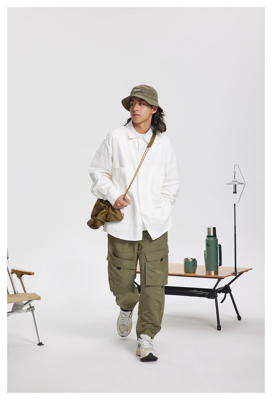 Model walking in a white oversized shirt with large chest pockets, olive cargo pants and a crossbody bag