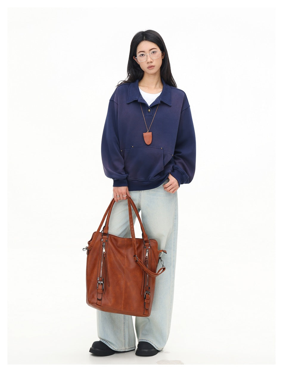Model wearing navy polo-collar sweatshirt over a white tee with light jeans, holding a brown tote bag
