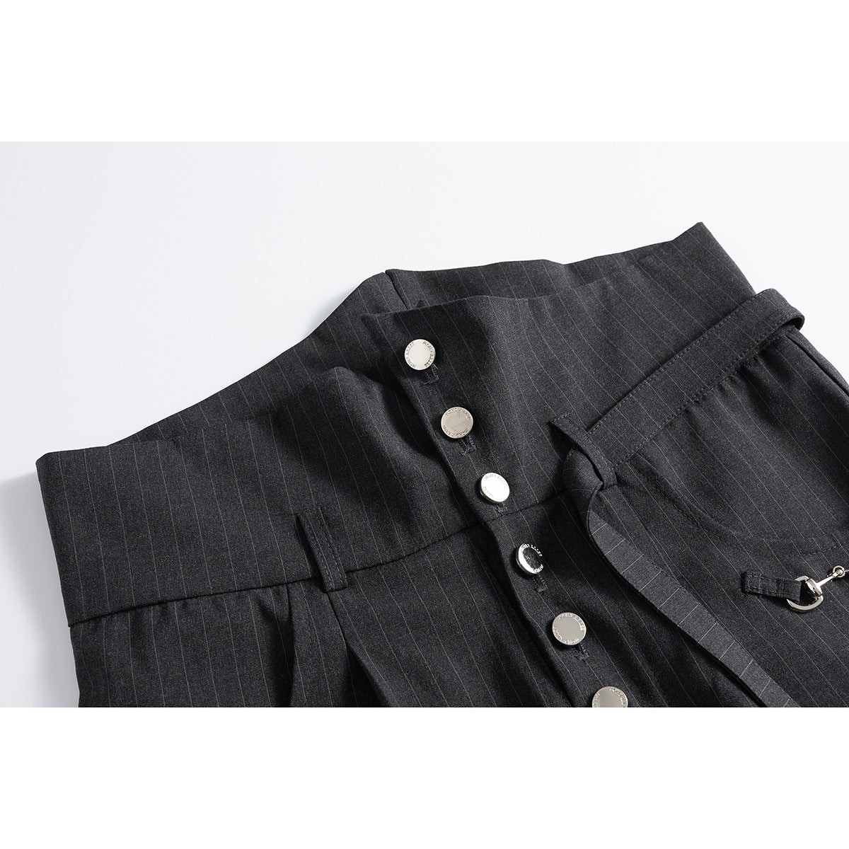 Close-up of charcoal pinstripe trousers showing the high waistband, silver buttons, belt loops and attached metal detail.