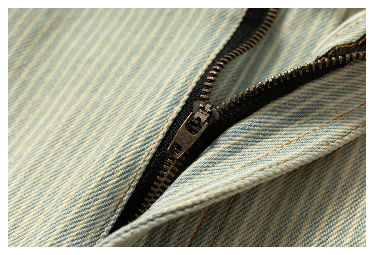 Close-up of an open metal zipper on pale blue and cream striped denim.