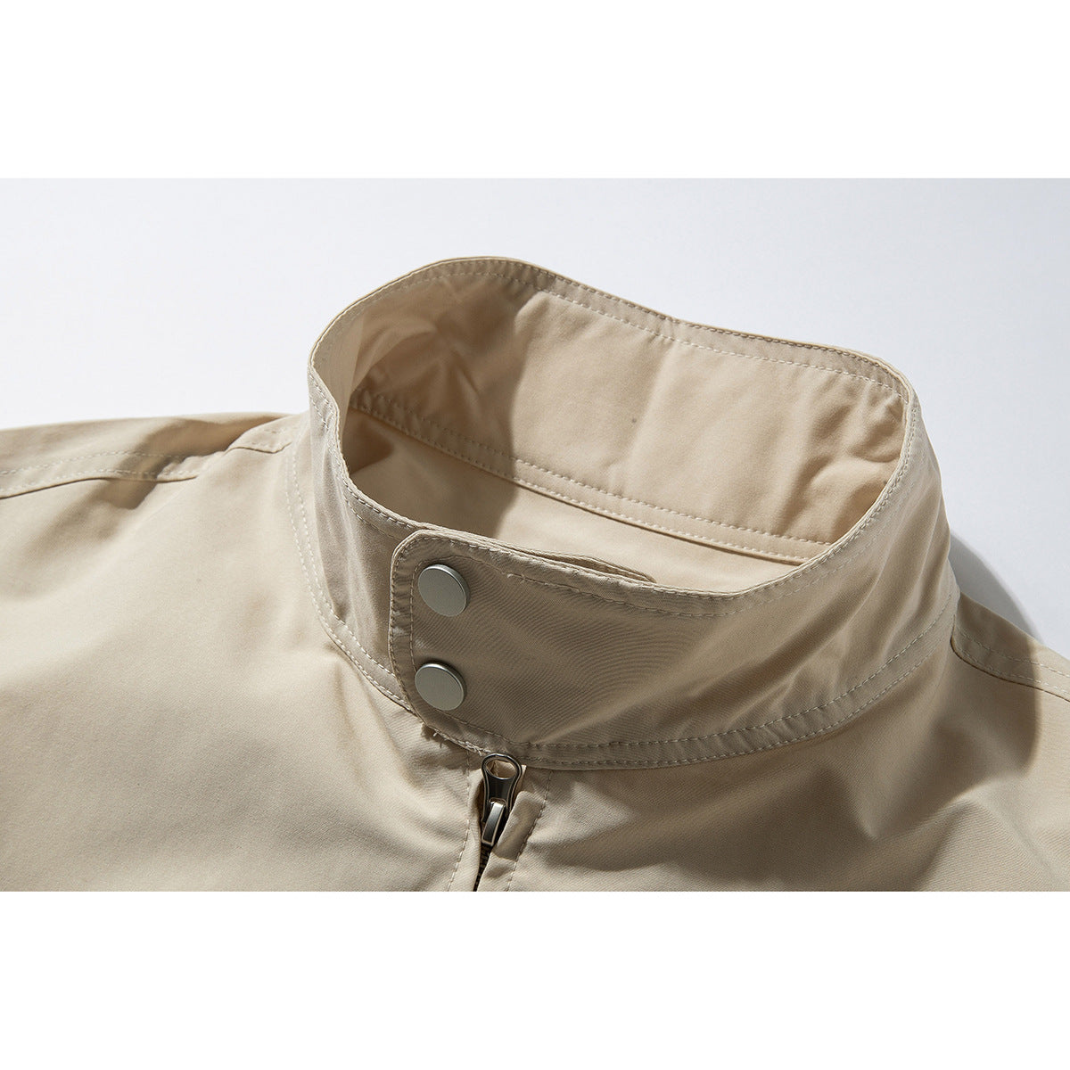 Close-up of a beige jacket’s raised stand collar, two metal snaps, and front zipper.