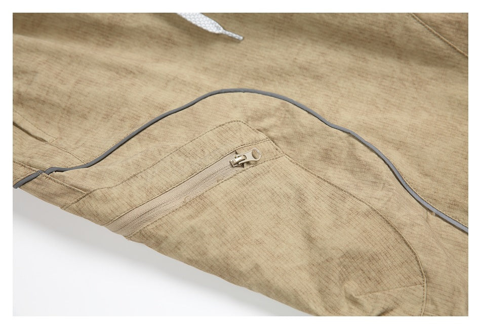 Close-up of a zippered pocket and curved gray piping on the tan pants.