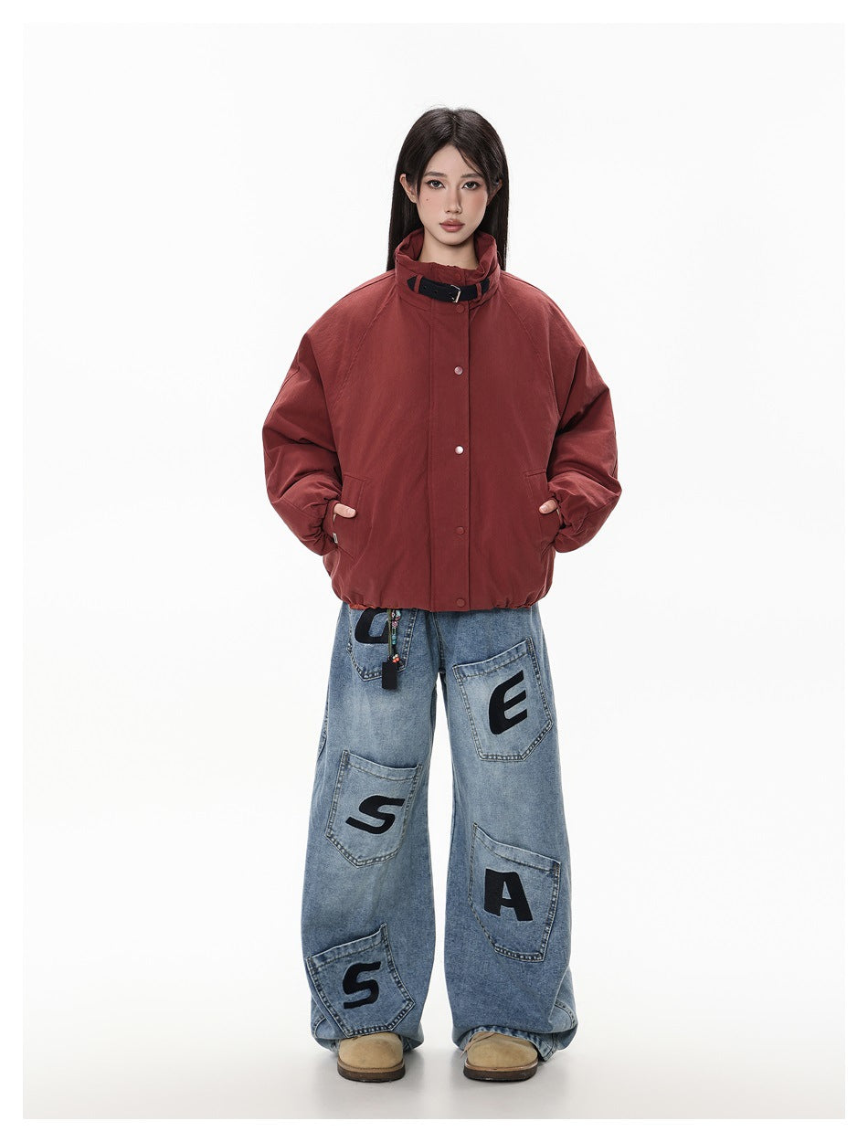 Model wearing burgundy buckle-collar jacket with hands in pockets and wide-leg jeans with black letter patches