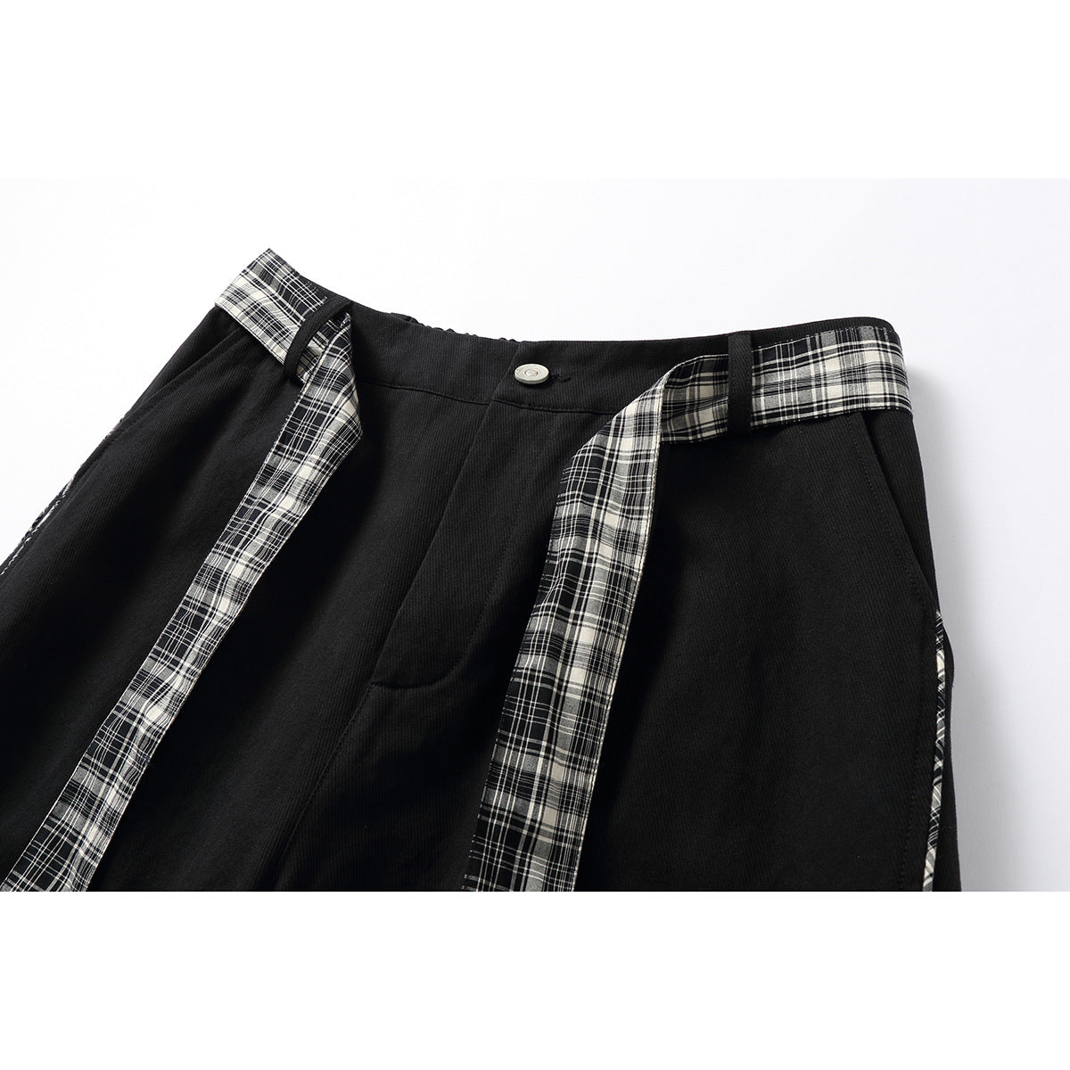 Close-up of black trousers with a silver button, plaid waistband sections, and long plaid ties.