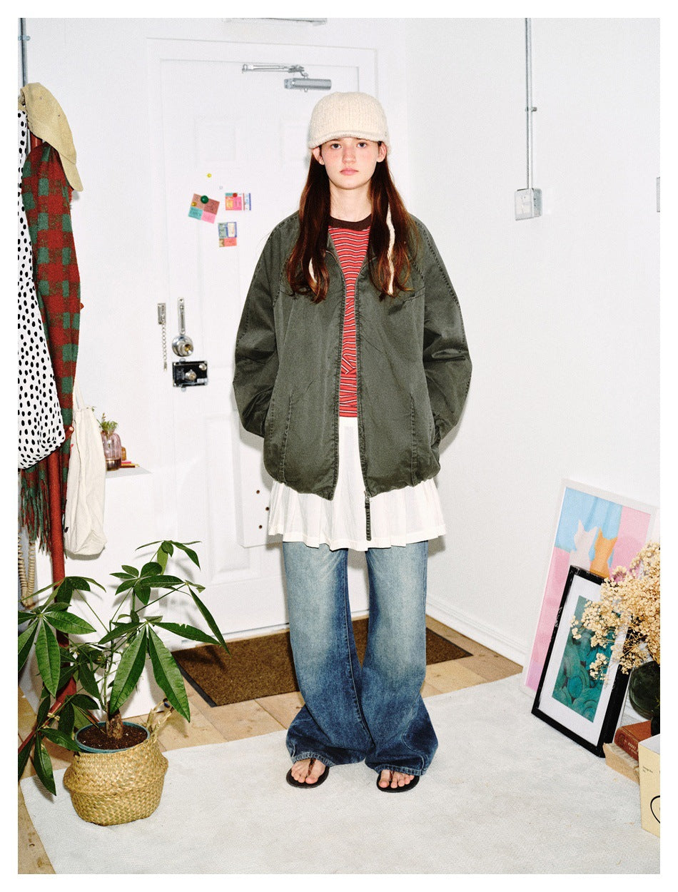 Front view of a model wearing a dark olive jacket with a red striped top, white skirt, wide-leg jeans and cream hat.
