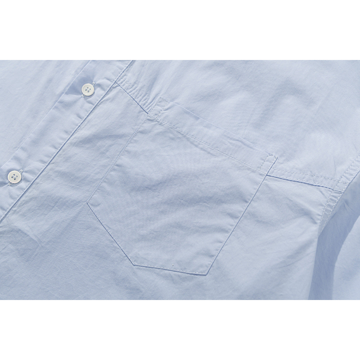 Close-up of a pale blue shirt's single chest pocket, stitching, and white front buttons.