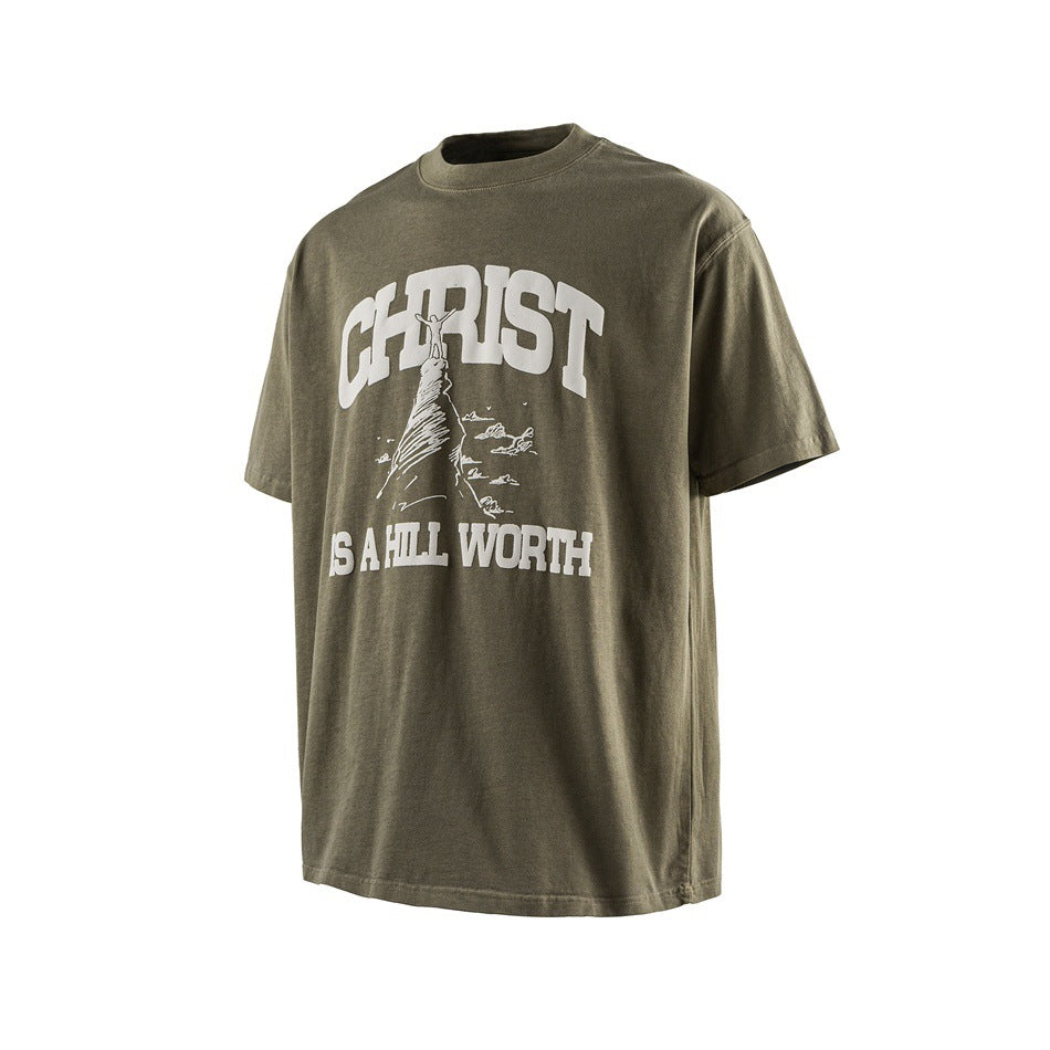 Washed green short-sleeve T-shirt with white 'CHRIST IS A HILL WORTH' hill graphic, angled front view