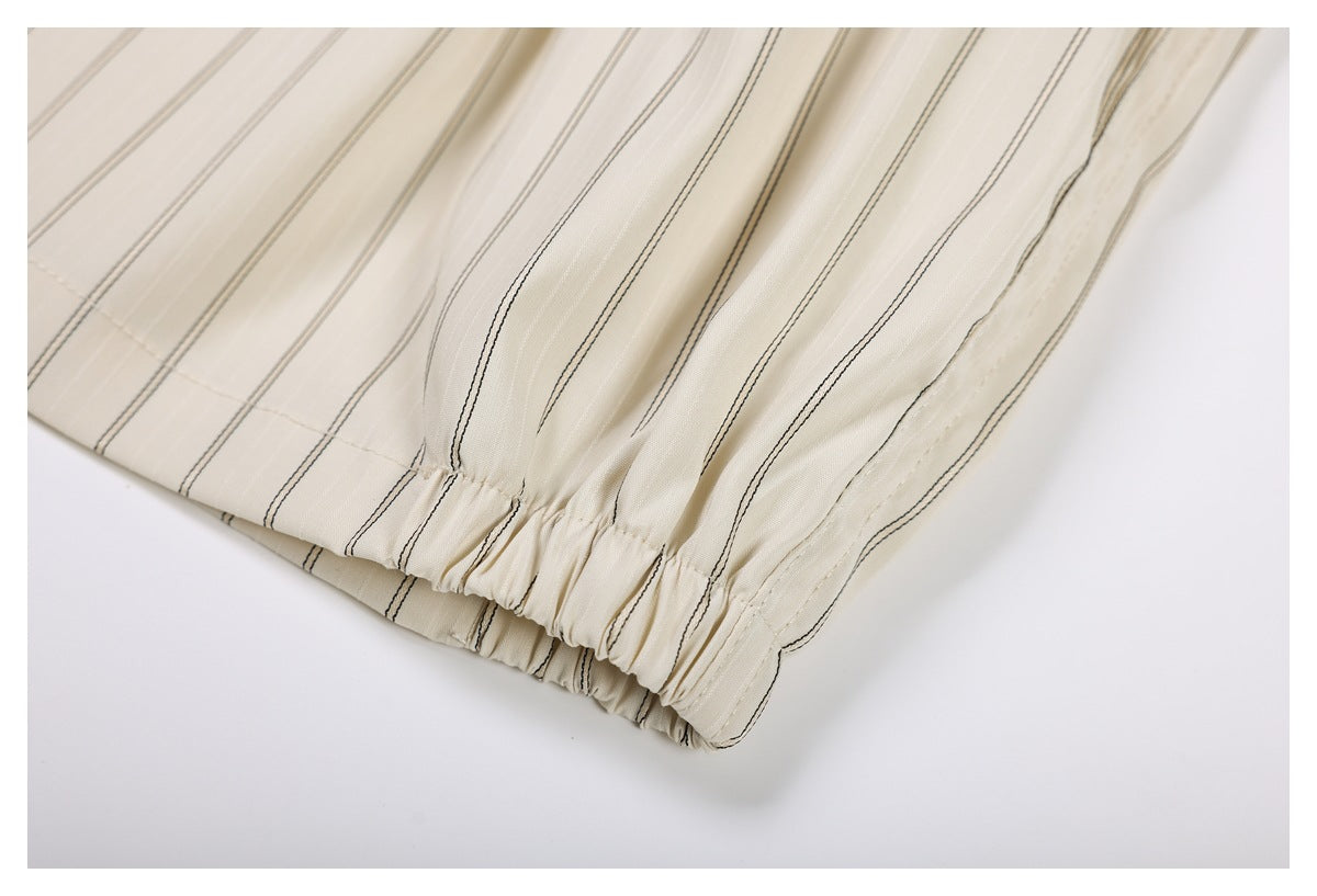 Close-up of gathered elastic edging on cream trousers with thin dark vertical stripes.