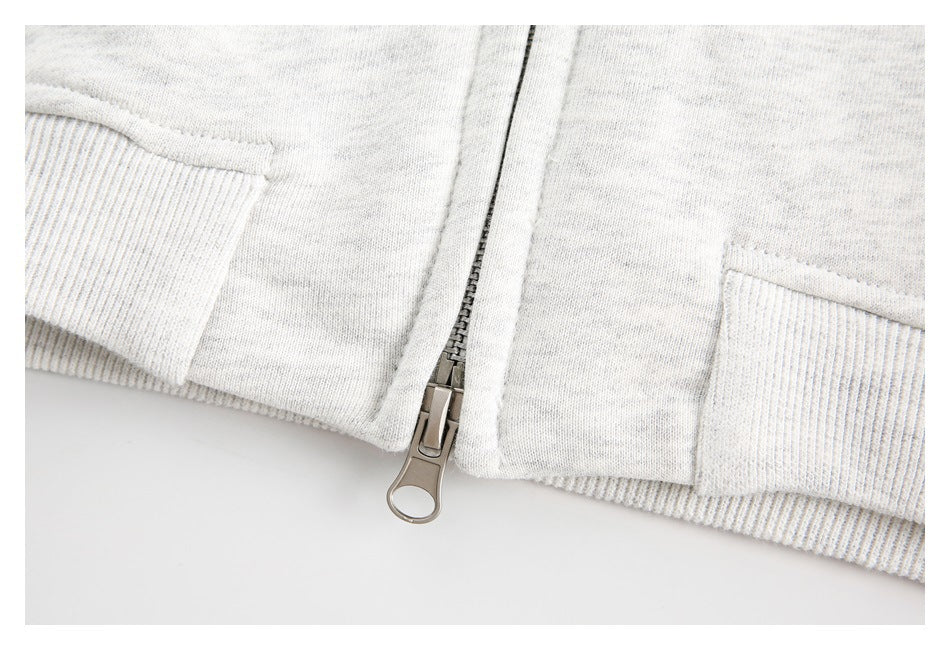 Close-up of a metal front zipper and ribbed hem on a light gray heathered sweatshirt.