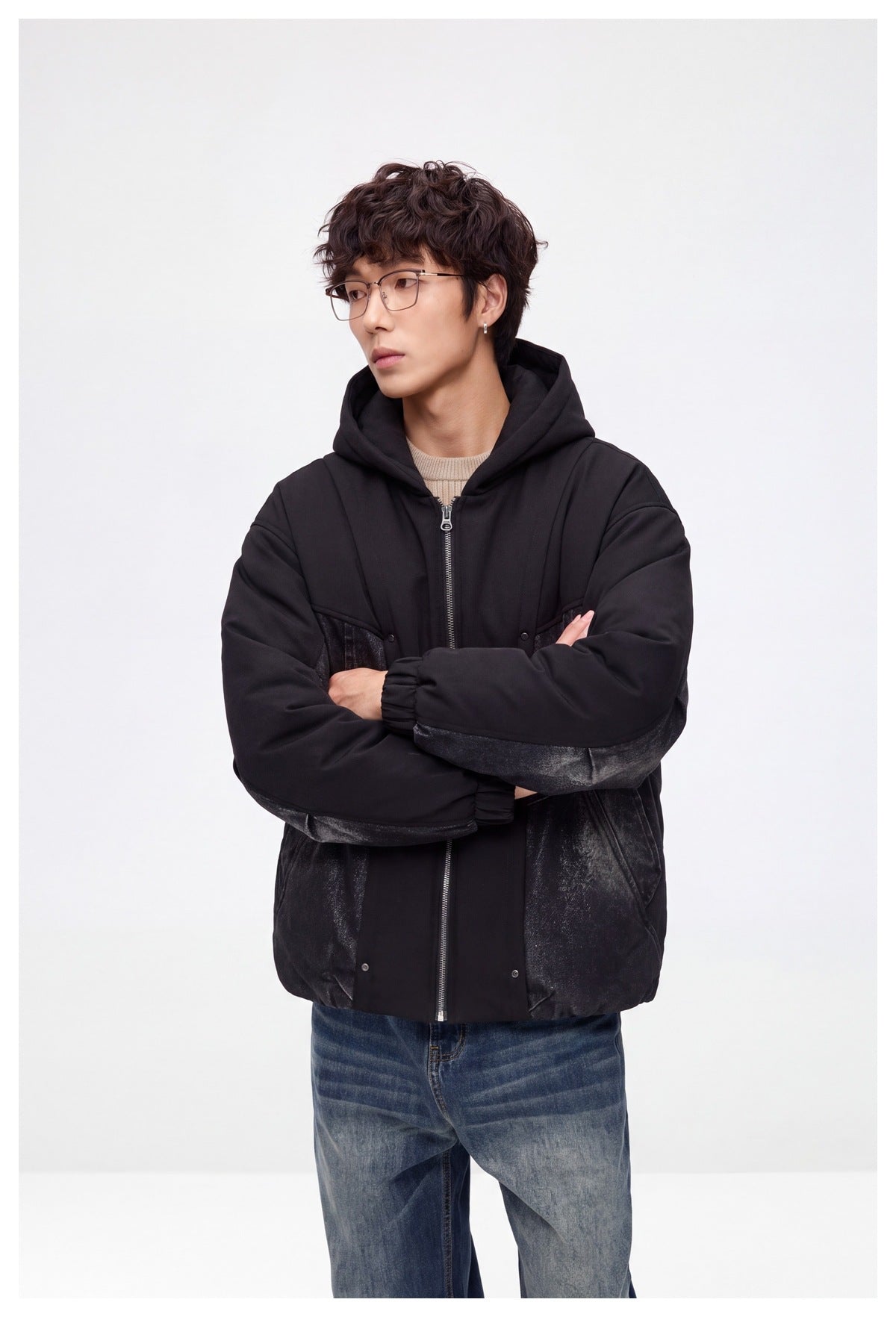 Model wearing a black hooded zip jacket with dark denim panels, shown from the front with arms crossed.