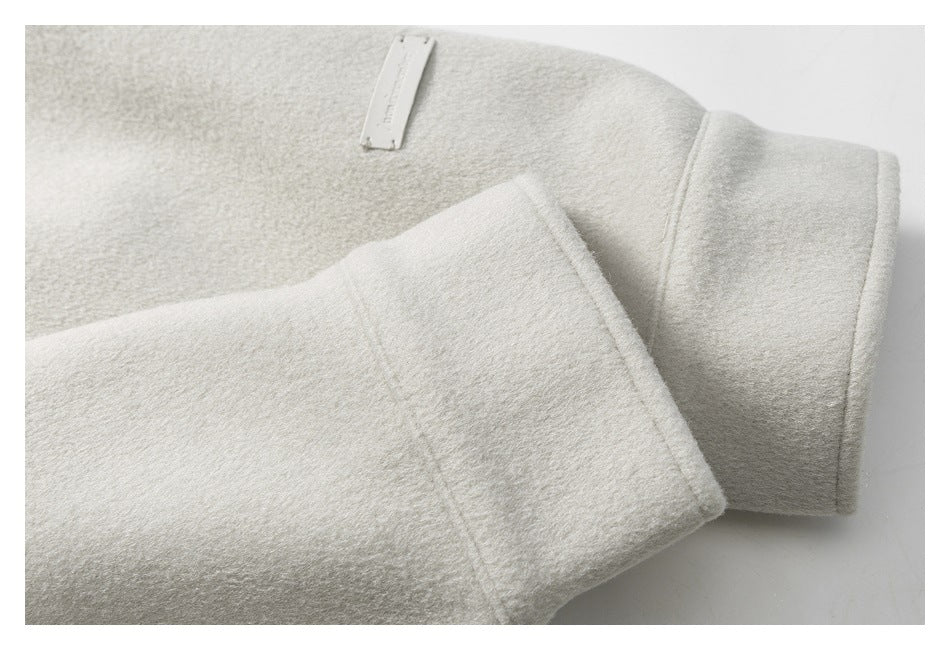 Close-up of an off-white coat sleeve cuff and a small rectangular metal nameplate.
