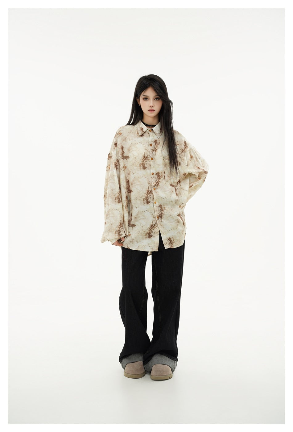 Front view of a model in an oversized cream and brown abstract-print shirt and black wide-leg jeans.