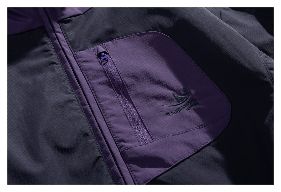 Close-up of the jacket's purple zip pocket with a small embroidered logo on dark navy fabric.
