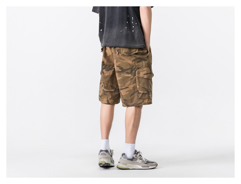 Person wearing khaki camouflage cargo shorts with a dark tee and gray sneakers, back view, cropped at the shoulders