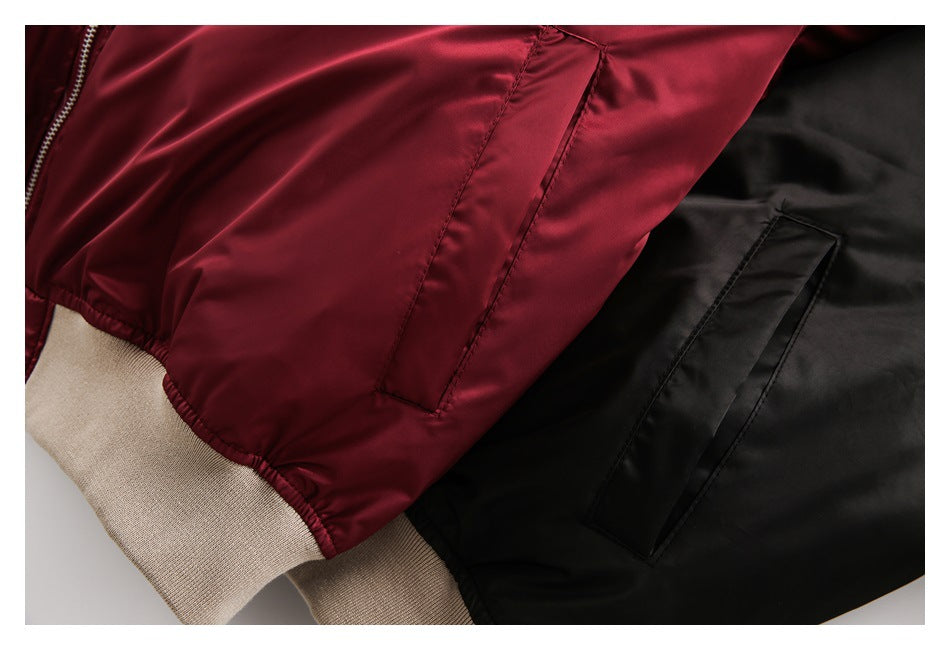 Close-up of burgundy and black bomber jacket pockets, seams, and beige ribbed hem.