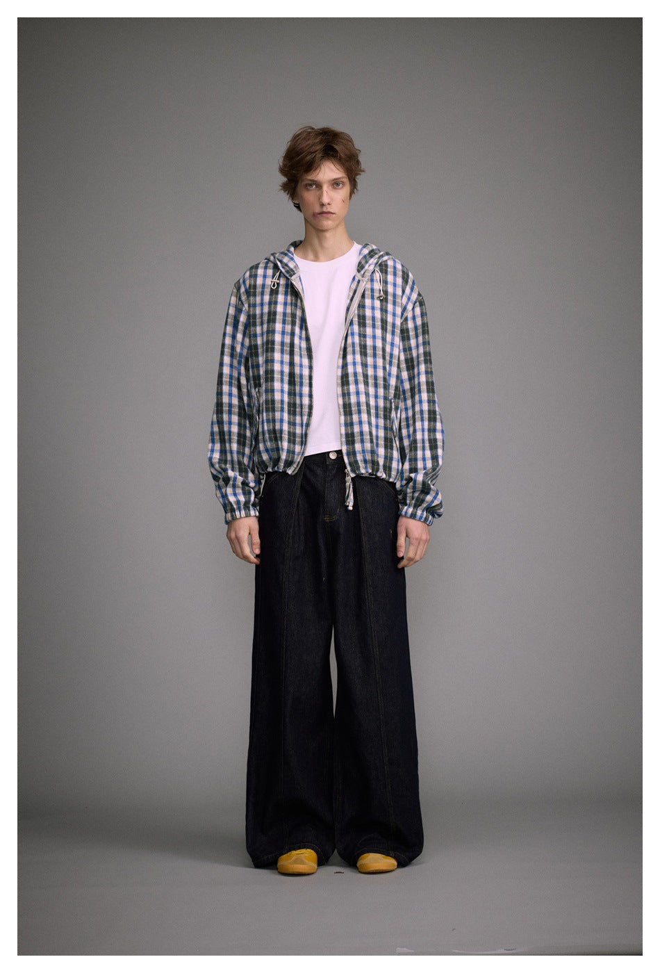 Model wearing an open blue plaid hooded jacket over a white tee with wide dark jeans and yellow shoes