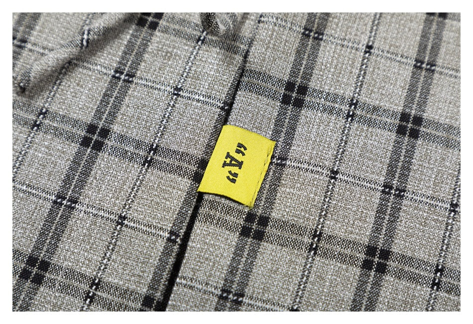 Close-up of a small yellow woven label with dark lettering on the gray plaid blouse.