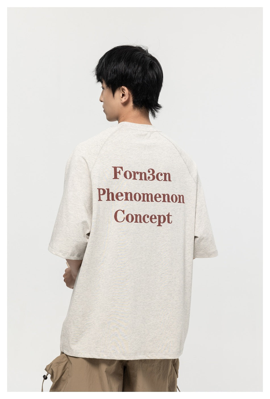 Model viewed from behind wearing an off-white T-shirt with large burgundy “Form3cn Phenomenon Concept” lettering.