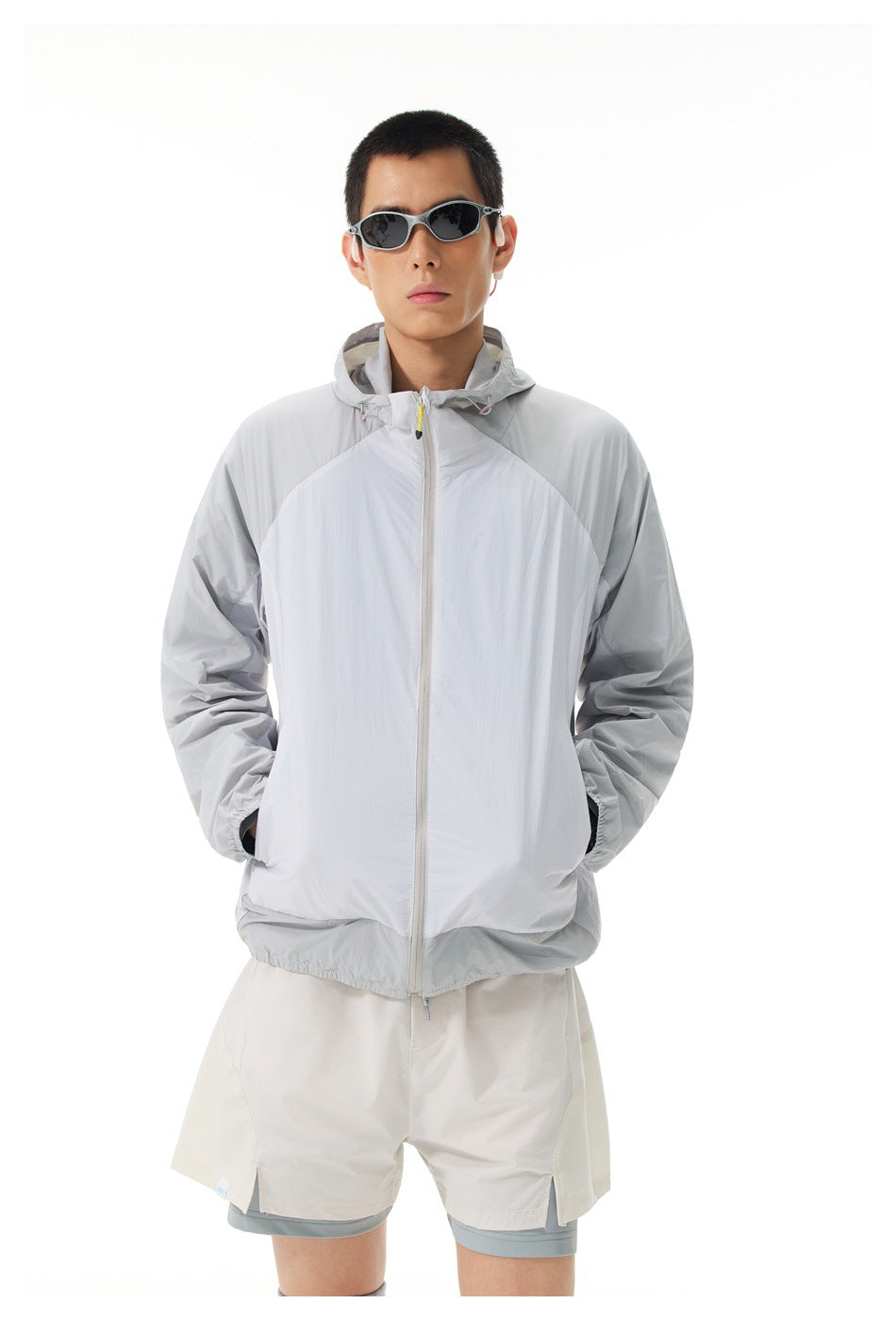Front view of a model wearing a light gray color-block hooded zip jacket and layered white shorts.