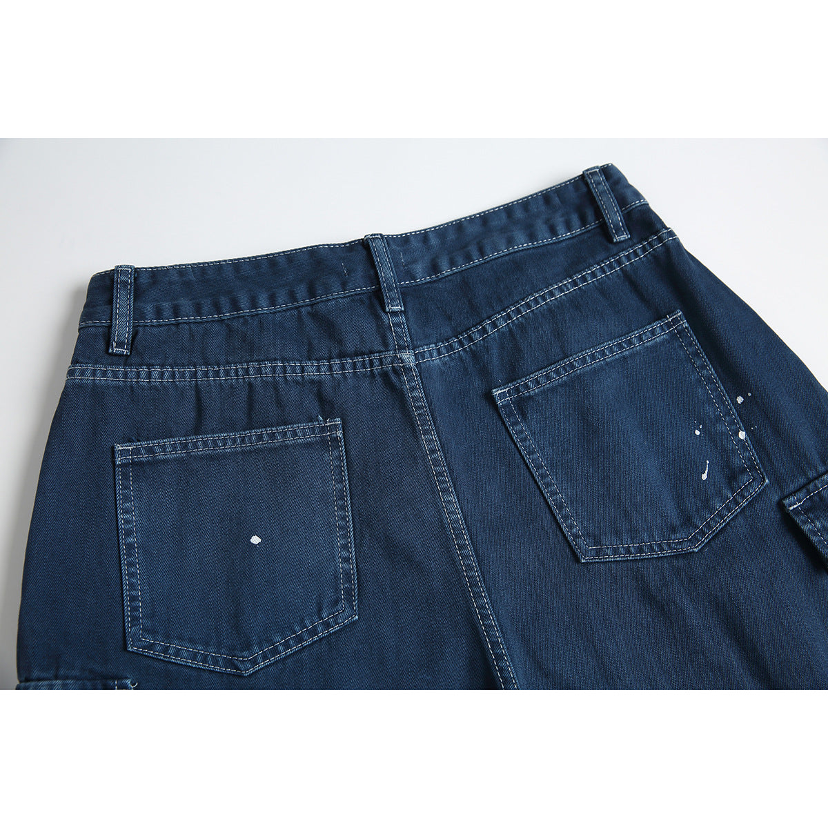 Close-up of the back of dark blue denim shorts with two patch pockets and scattered white paint-like speckles.
