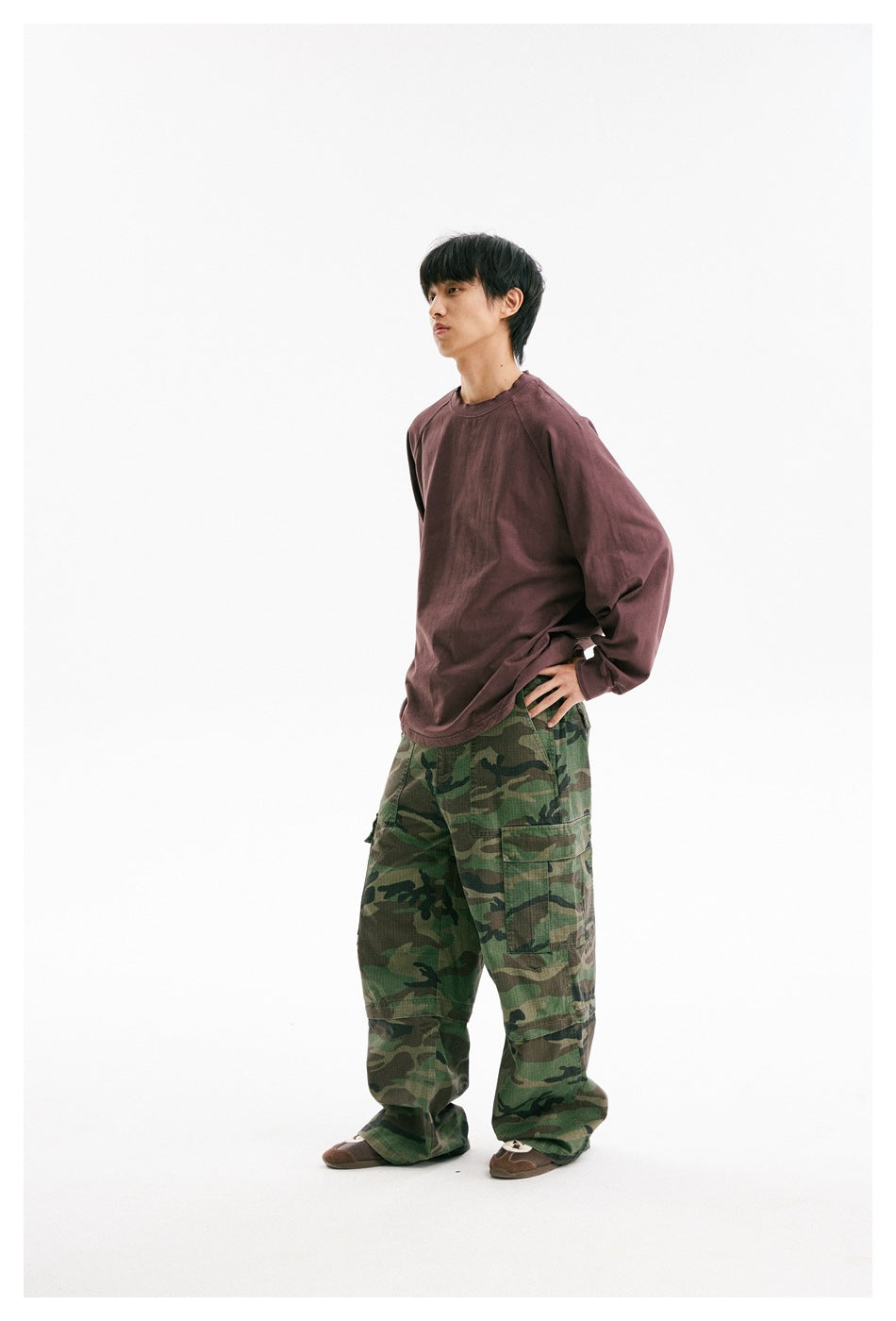 Male model wearing a loose muted-plum long-sleeve shirt and green camouflage cargo pants.