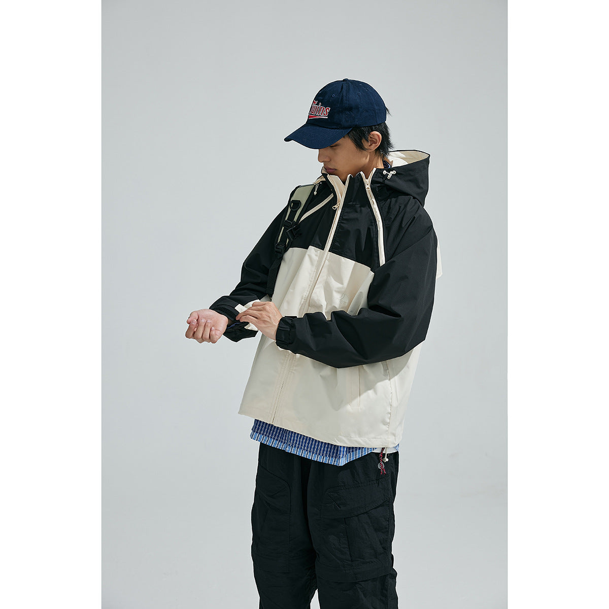 Model wearing a black-and-cream hooded jacket, shown from the front while adjusting a sleeve.