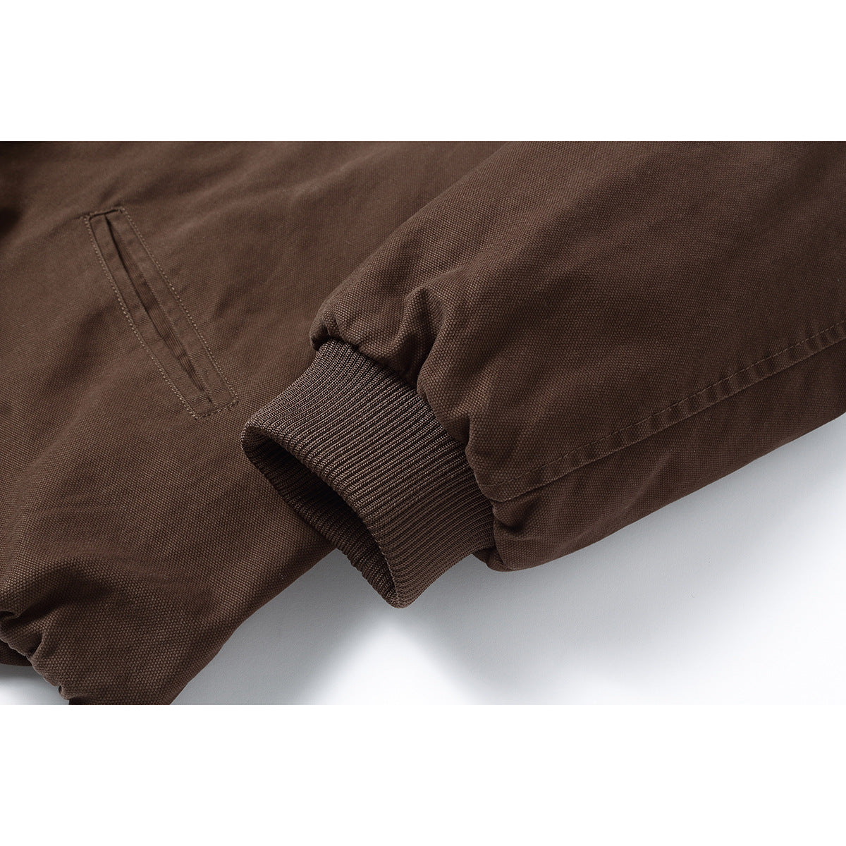 Close-up of a dark brown jacket sleeve with a ribbed cuff and a narrow welt pocket.