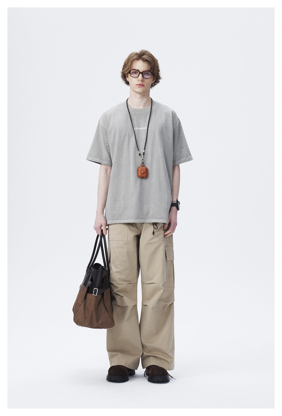 Model wearing gray oversized t-shirt with khaki cargo pants and a brown tote bag, front view