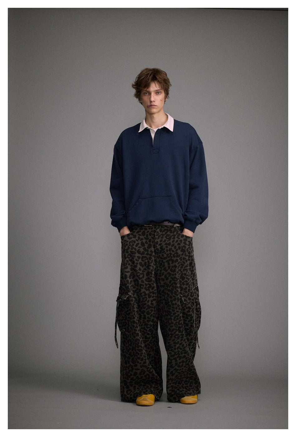 Full-length front view of a model wearing a navy pullover with a pale pink collar and dark leopard-print cargo pants.