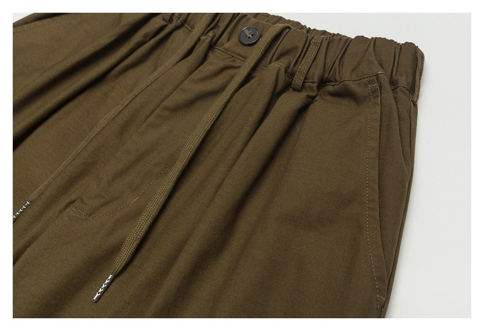 Close-up of brown pants at the front, showing the buttoned elastic waist, drawstring, and pocket opening.