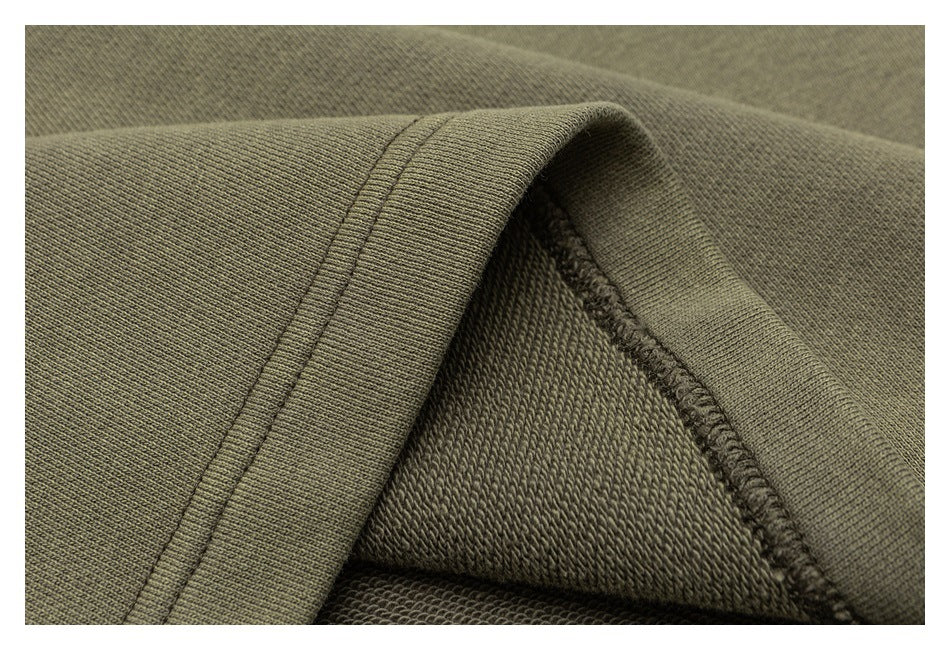 Close-up of an olive sweatshirt seam and folded hem, showing the inner knit and overlock stitching.