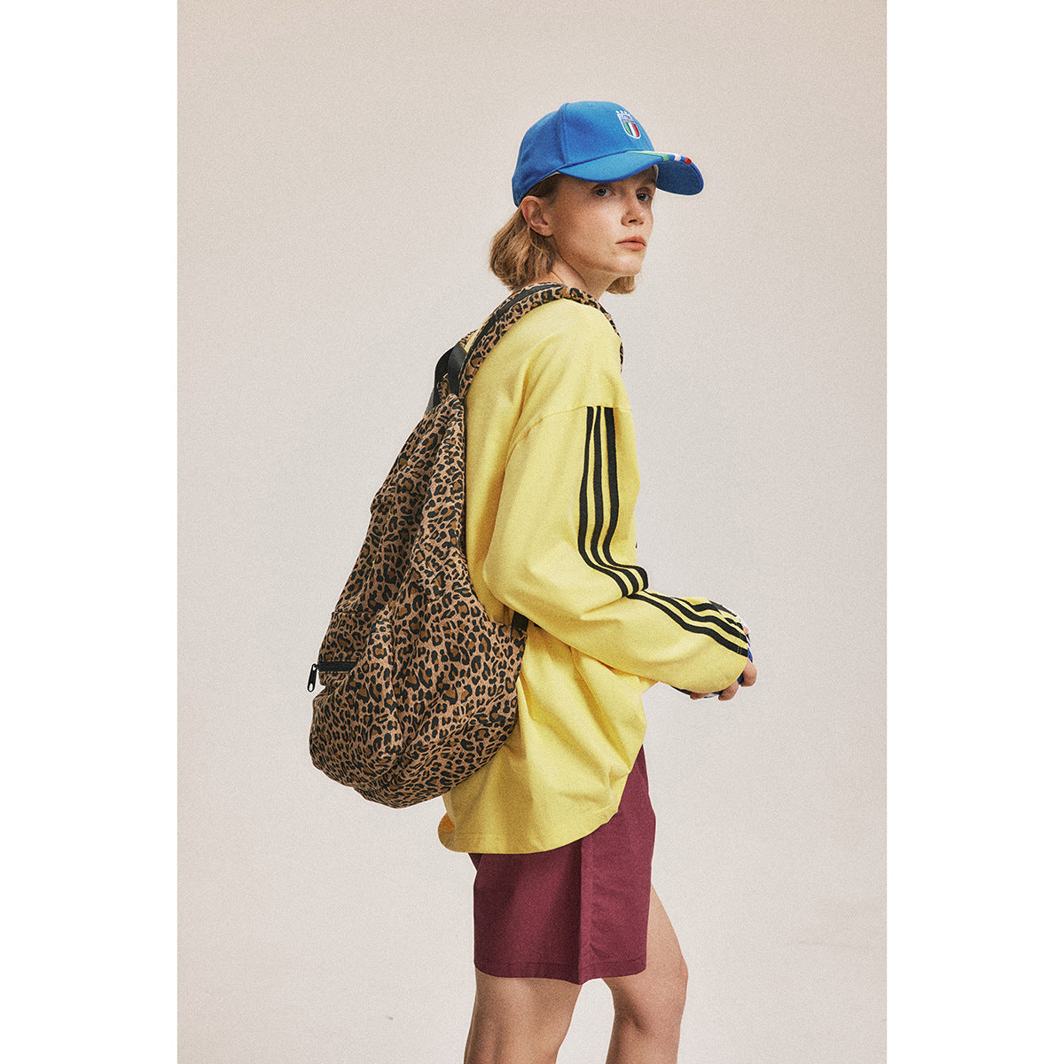 Side view of a model wearing a yellow striped sweatshirt and burgundy shorts, with a leopard-print backpack.