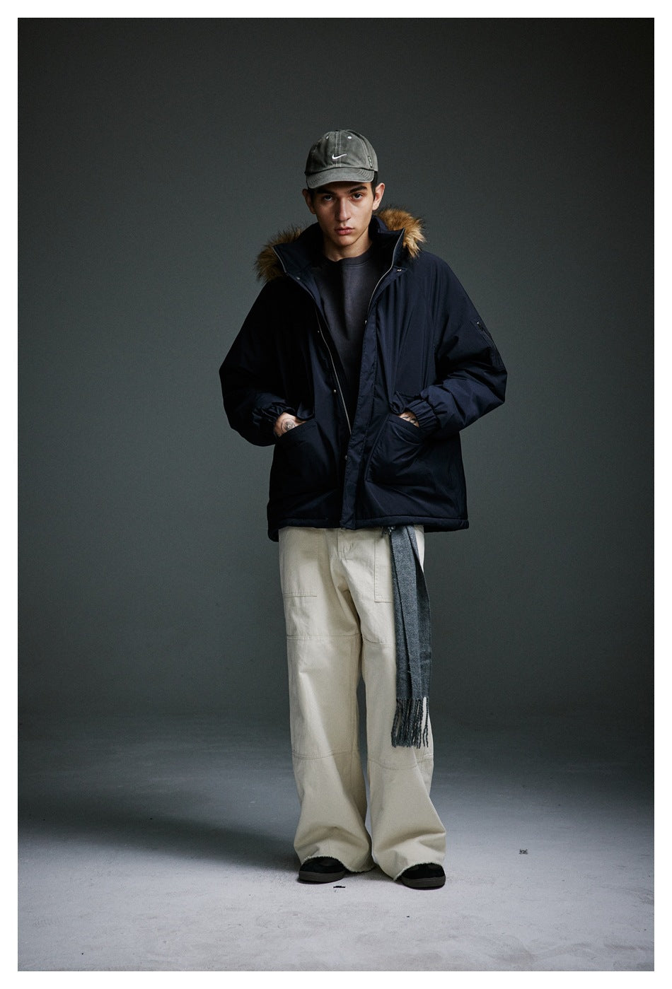 Full-length front view of a model wearing a navy fur-trimmed parka with beige wide-leg trousers.
