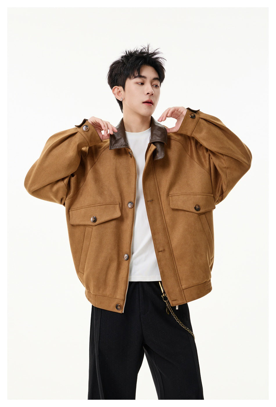 Model wearing a khaki suede-look jacket with brown collar over a white tee and black trousers, hands raised at the collar