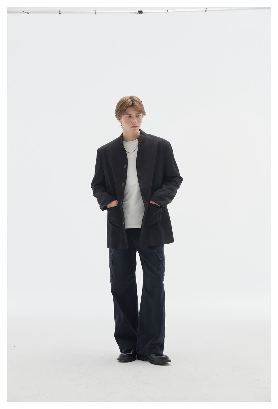 Model with hands in the pockets of a black stand-collar button jacket, styled with a white shirt and wide black cargo pants.