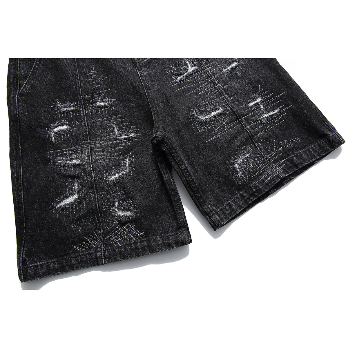 Close-up of black denim shorts legs with distressed patches, contrast stitching, and finished hems.