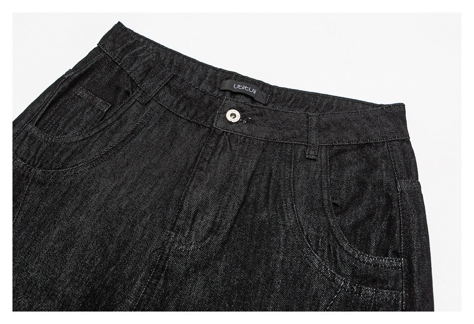 Close-up of the black trousers' front waistband, button, pleats and curved pockets.