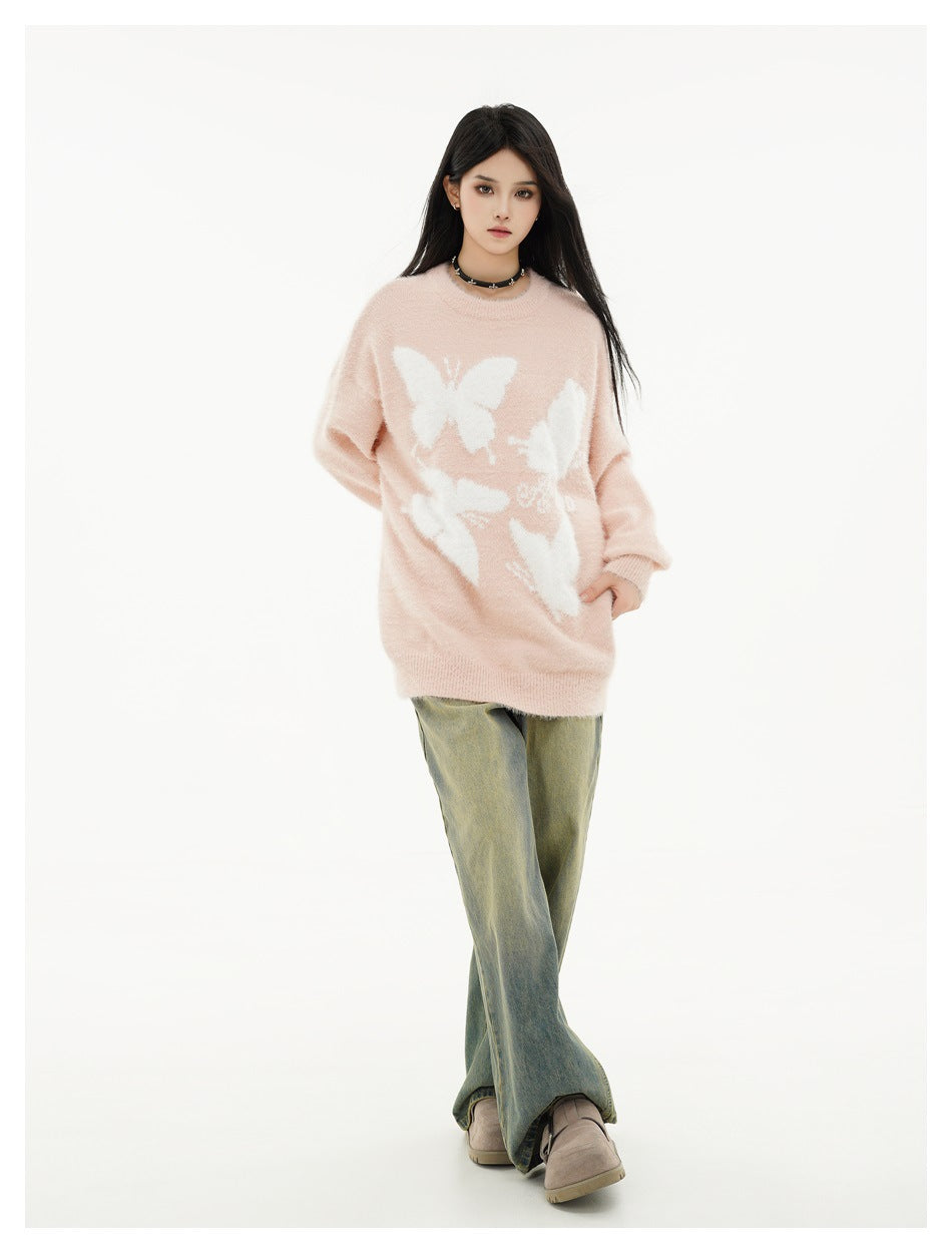 Model wearing an oversized blush-pink sweater with large white butterfly motifs, olive wide-leg jeans and taupe shoes.