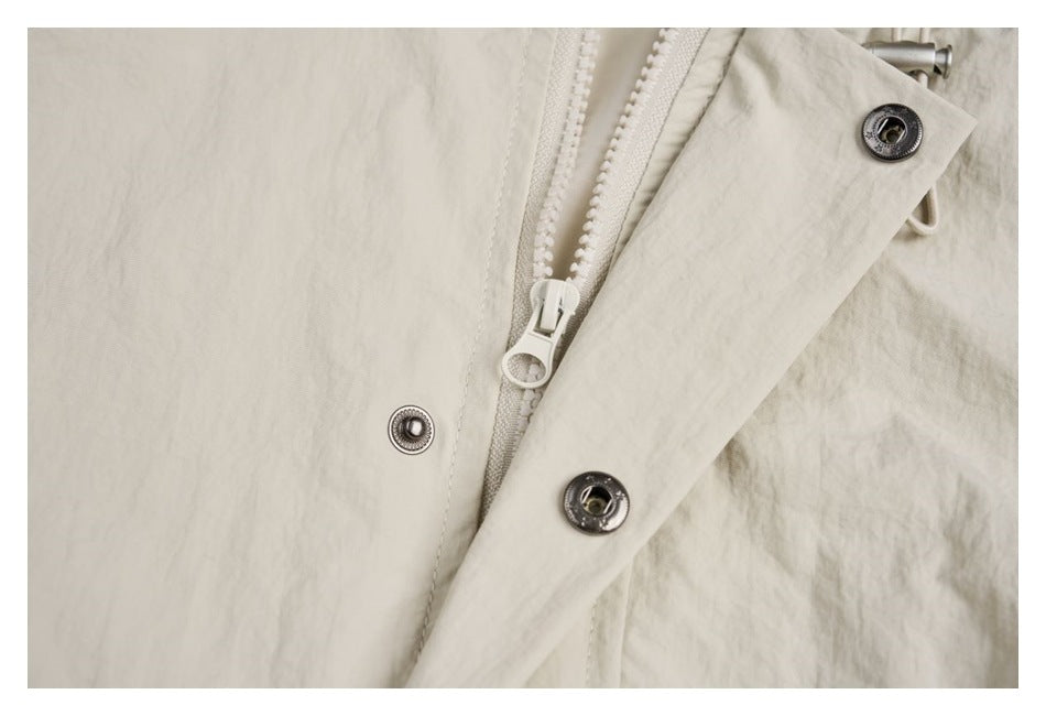 Close-up of an ivory garment showing a white zipper and dark metal snap fasteners.