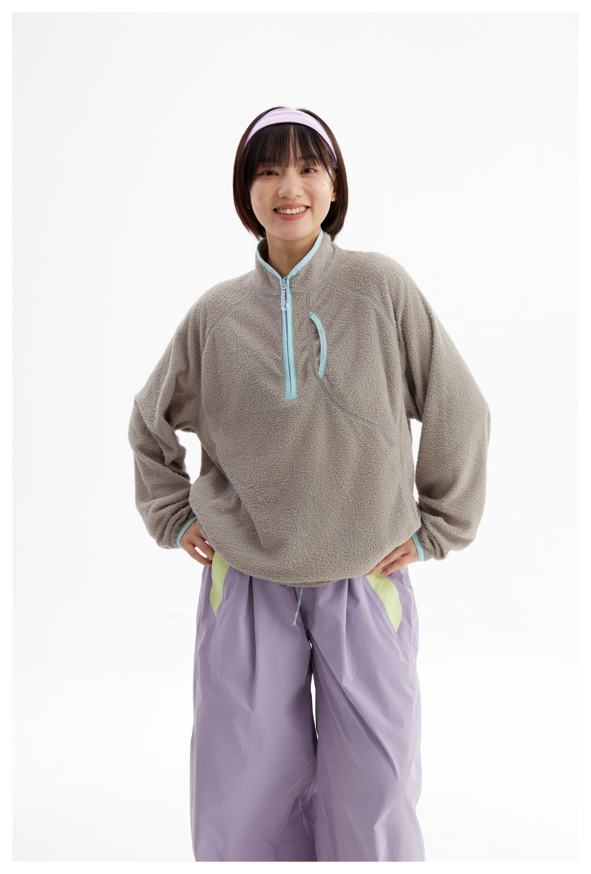 Front view of a model wearing a taupe fleece pullover with aqua trim and lavender pants.