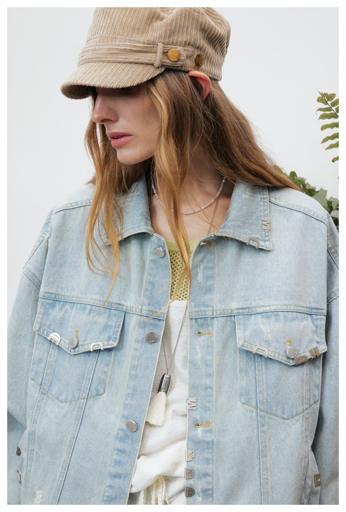 Close view of a model wearing an oversized light-wash distressed denim jacket with flap pockets and metal accents.