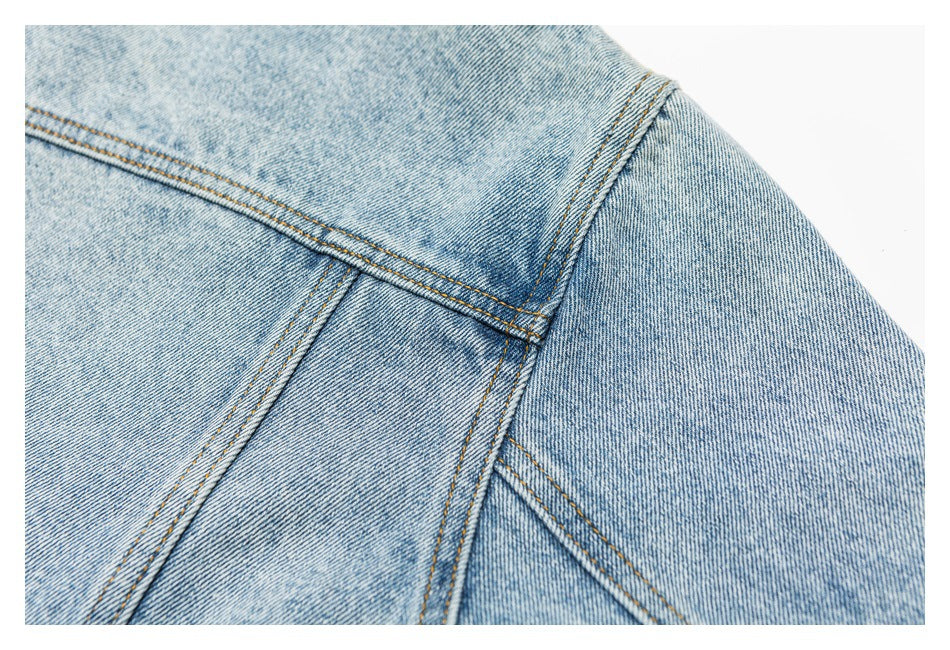 Close-up of the back shoulder area of a light blue denim jacket, showing the yoke and intersecting seams.