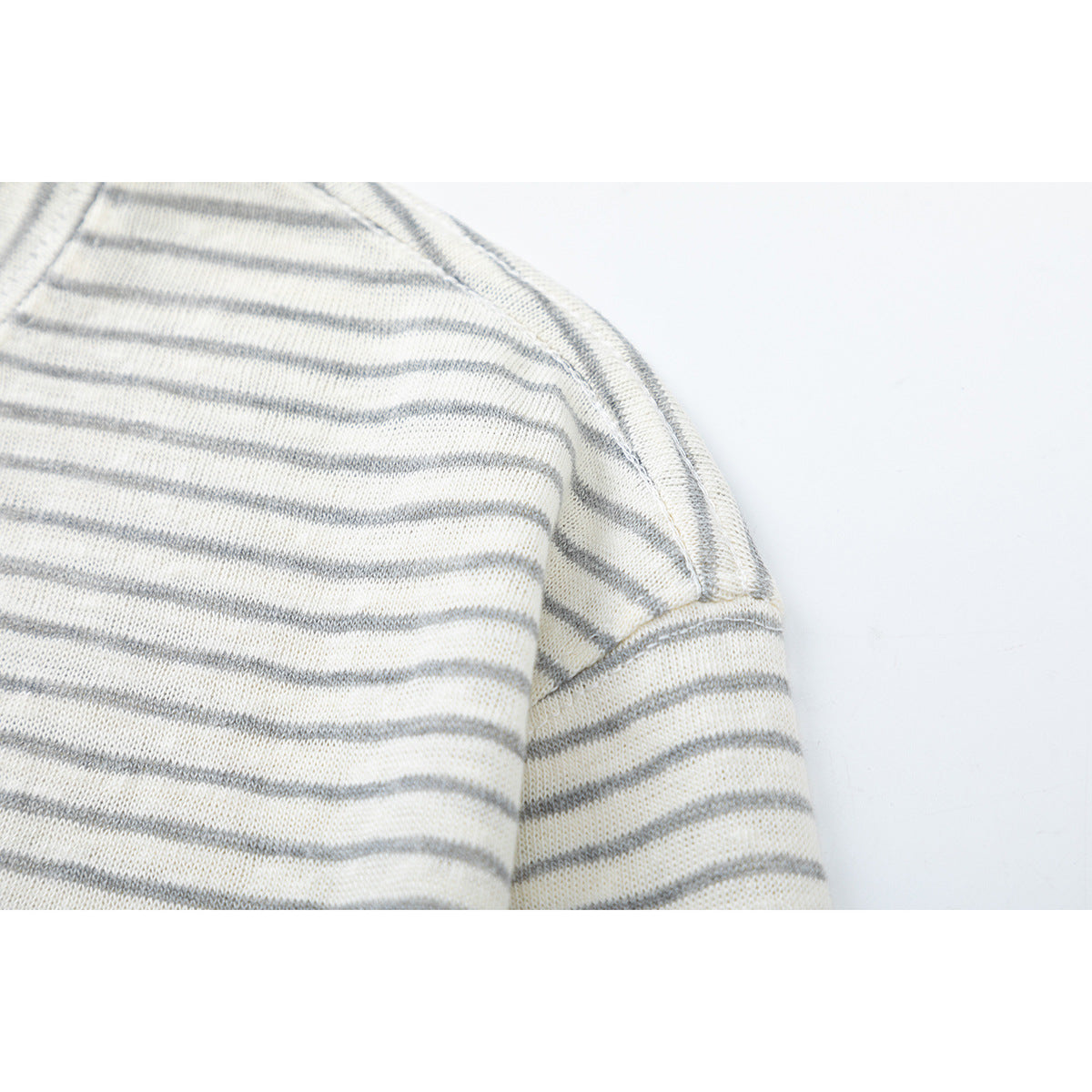 Close-up of the shoulder seam and sleeve on a cream shirt with narrow gray stripes.