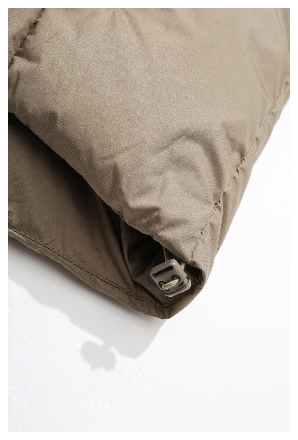 Close-up of the taupe jacket hem with a cord and plastic adjustment toggle.