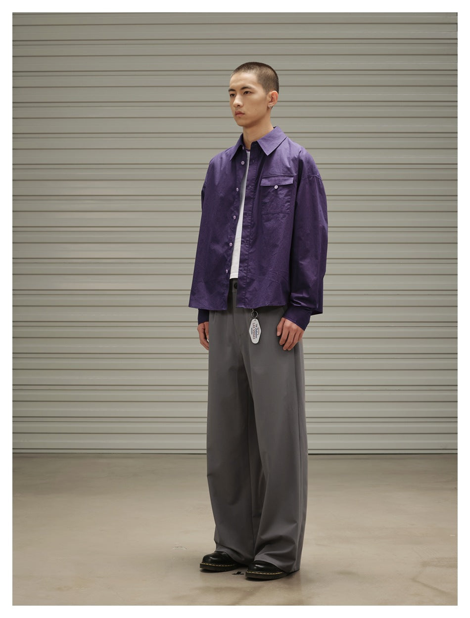 Three-quarter view of a model wearing a purple button-up overshirt, white T-shirt, and wide gray trousers.