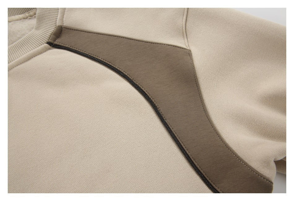 Close-up of a beige sweatshirt with a taupe curved panel and dark seam piping.