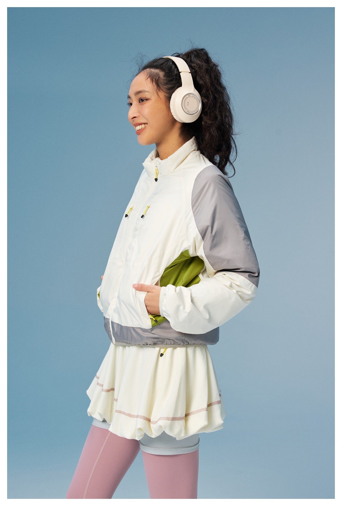 Three-quarter view of a woman wearing a white zip jacket with gray sleeves and lime side panels, paired with a white skirt.