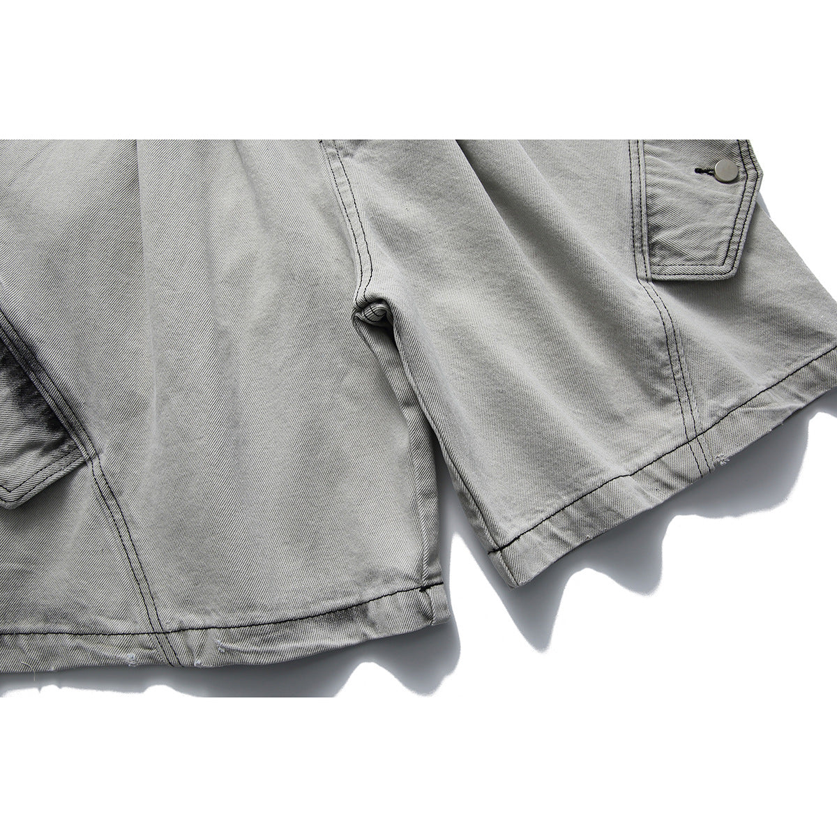 Close-up of gray washed denim shorts showing a pocket, side seams and a wide hem.