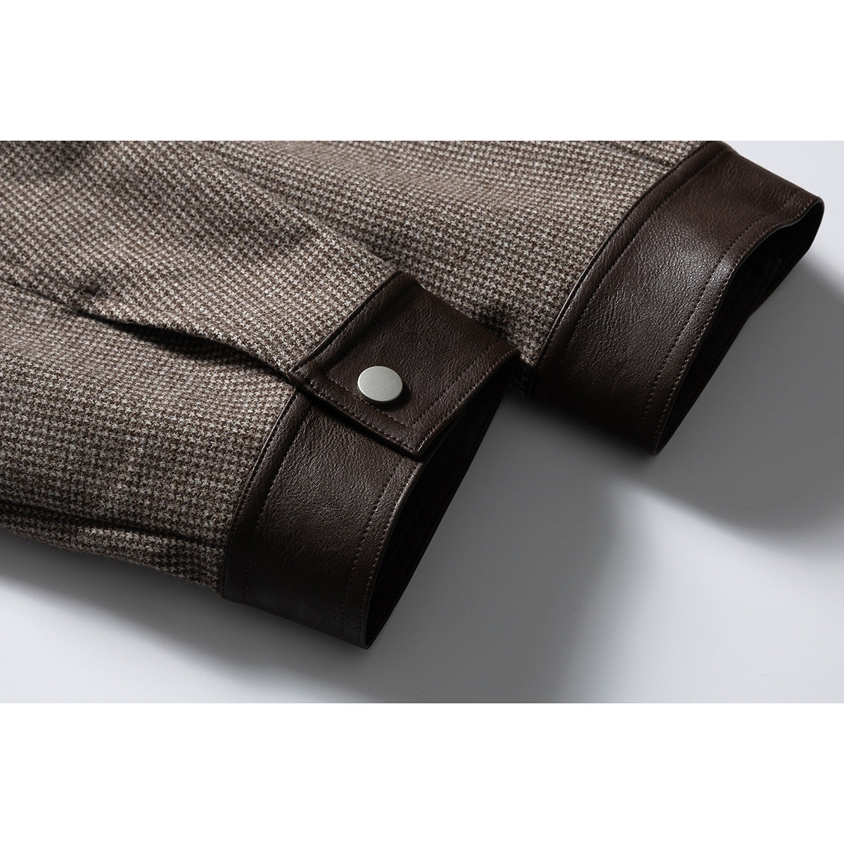 Close-up of a houndstooth jacket sleeve with a dark brown cuff and silver snap closure.
