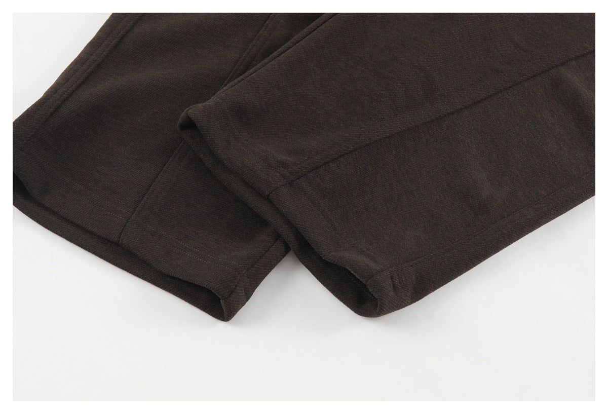 Close-up of the stitched hems of dark brown pants, with the legs folded over each other.